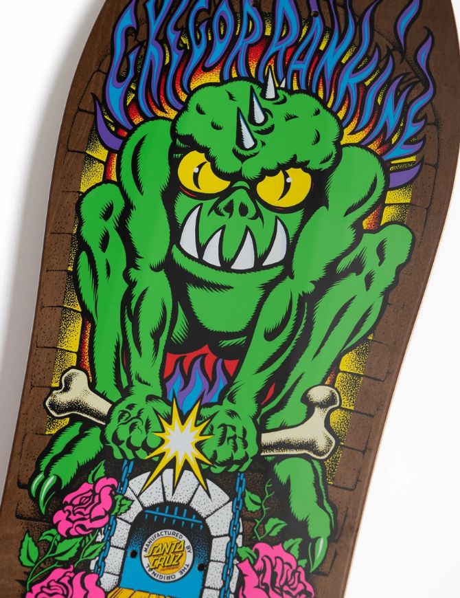 A close-up of a skateboard deck featuring a colorful graphic of a green monster with yellow eyes, blue flames, pink roses, and a Santa Cruz logo at the bottom.